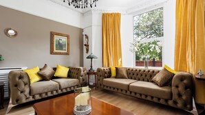 A living room with two tufted sofas, a wooden coffee table, a framed picture on the wall, and a window with yellow curtains.