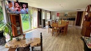 A spacious living area with a wooden dining table, a TV mounted on the wall, and a kitchen in the background. - Large, comfortable villa in the Cévennes, mountains, lakes and rivers. Pets welcome! (concoules)
