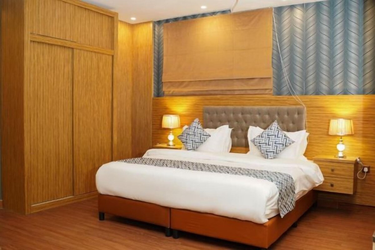 Ein Schlafzimmer mit einem Holzkleiderschrank, einem gepolsterten Kopfteil, zwei Nachttischlampen und einem Bett mit gemusterten Kissen.