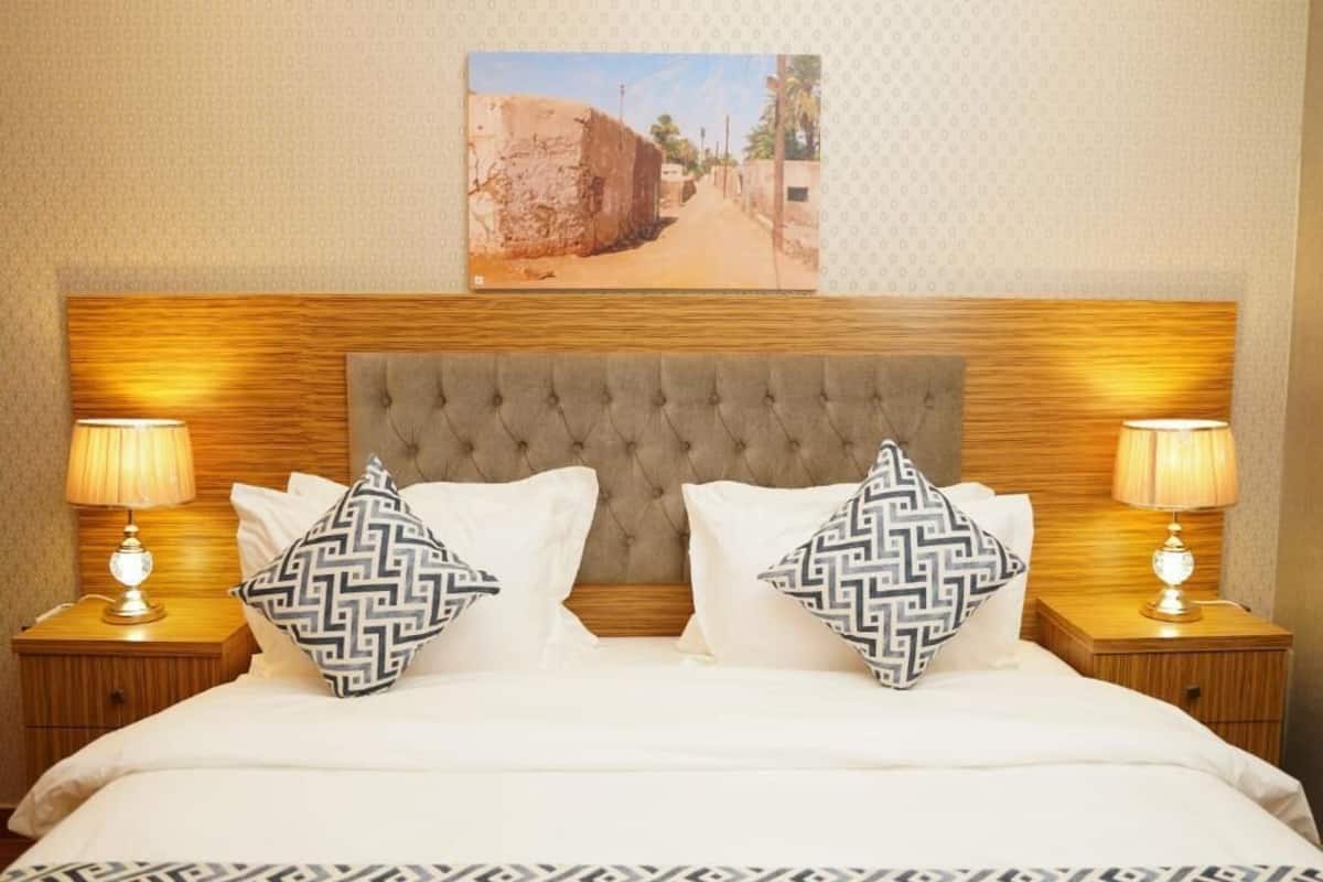 A neatly made bed with a tufted headboard, two patterned pillows, and two bedside lamps on wooden nightstands.