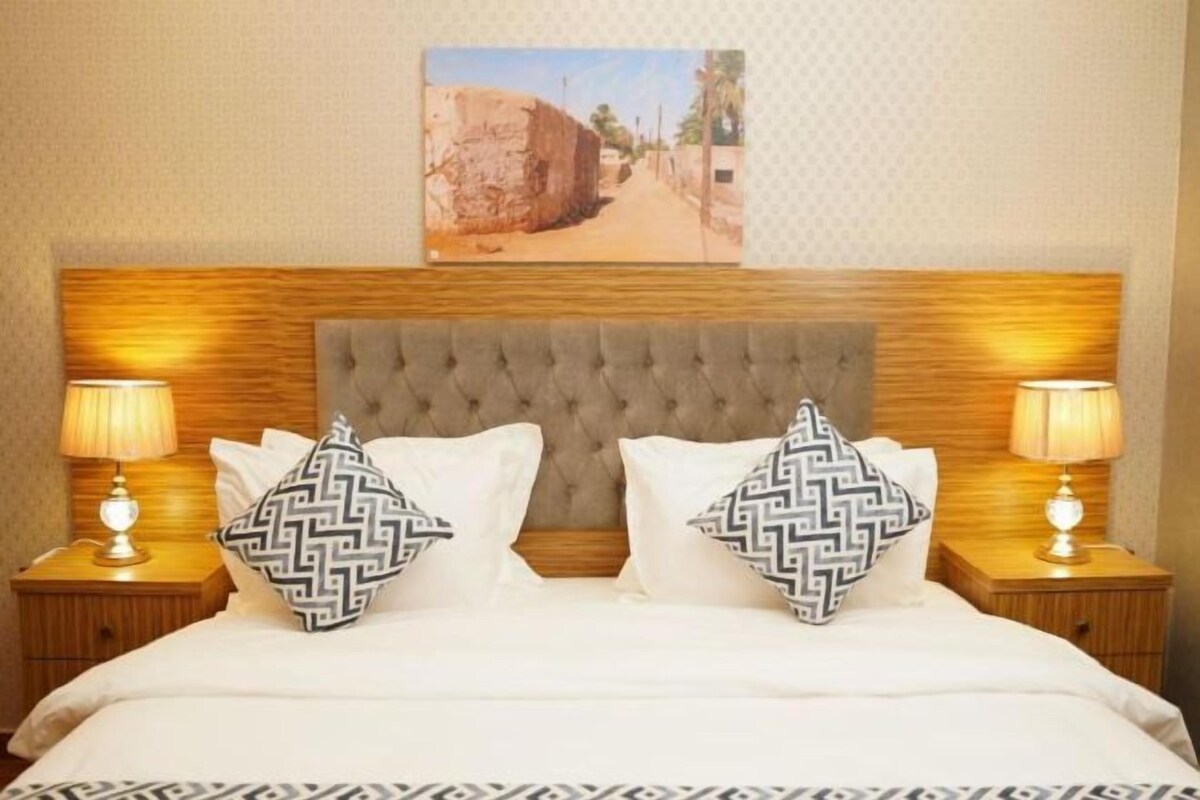 Una cama con cabecera capitonada, dos lámparas de noche y almohadas estampadas.