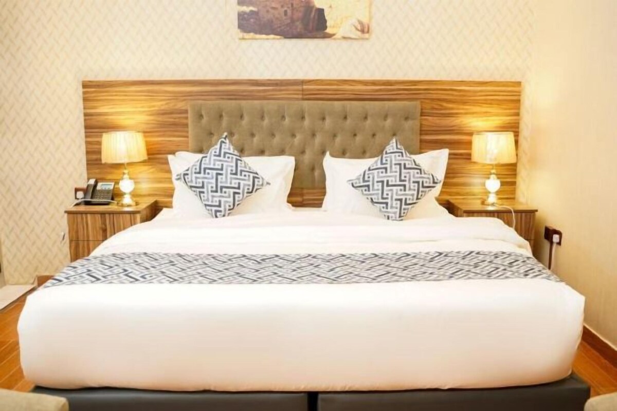 Una cama bien tendida con una colcha estampada, dos almohadas decorativas y dos lámparas de noche.