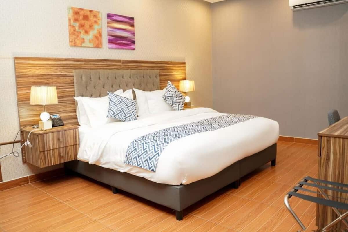 A modern hotel room with a large bed, wooden headboard, two bedside lamps, and artwork on the wall.