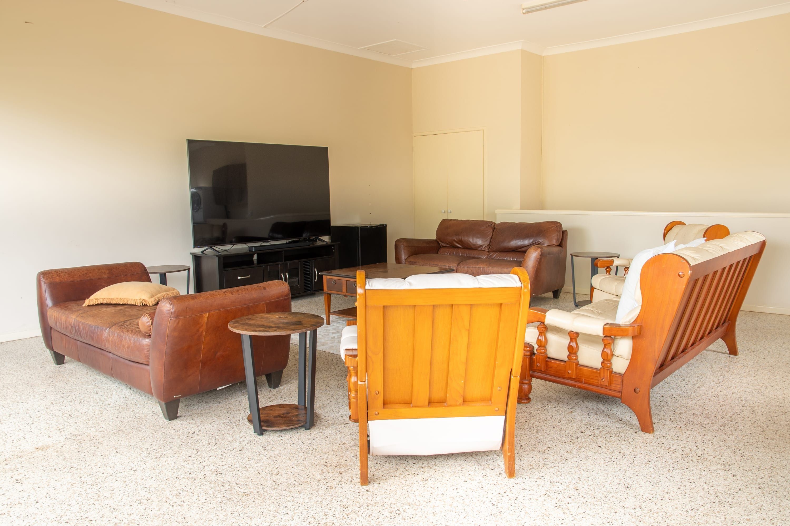 A living room with a brown leather sofa, a wooden armchair, a small round table, and a television on a stand.