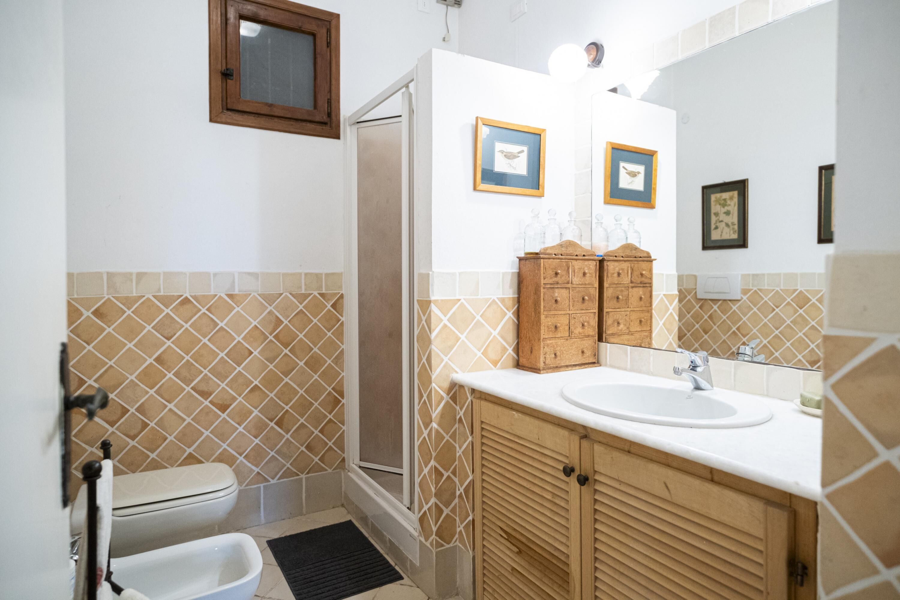 Une salle de bain comprenant des toilettes, une douche, un lavabo, des meubles en bois et des tableaux encadrés accrochés au mur.