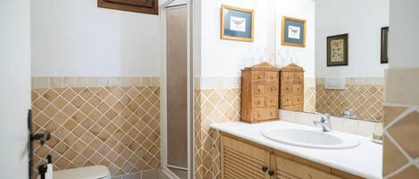 Une salle de bain comprenant des toilettes, une douche, un lavabo, des meubles en bois et des tableaux encadrés accrochés au mur.