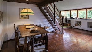 A dining area with a wooden table, chairs, and a hanging lamp. There is a staircase leading to an upper level.