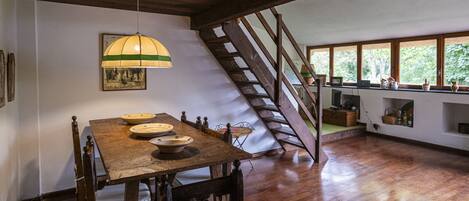 A dining area with a wooden table, chairs, and a hanging lamp. There is a staircase leading to an upper level.