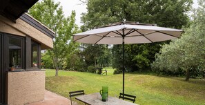 En udendørs patio med et bord, stole og en stor parasol, samt en grøn kande.