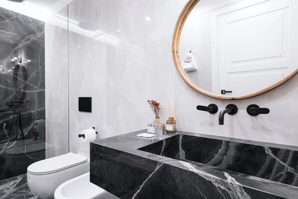 A modern bathroom with a marble sink, a toilet, and a shower.
