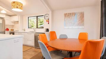 A modern kitchen with white cabinets, a dining area with orange chairs, a clock, and a map on the wall.