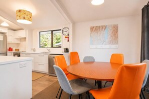 Une cuisine moderne avec des meubles blancs, un coin repas avec des chaises orange, une horloge et une carte accrochée au mur.