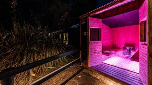 Eine Holzsauna mit Bank und Tisch, umgeben von Holzpflanzung und Vegetation.
