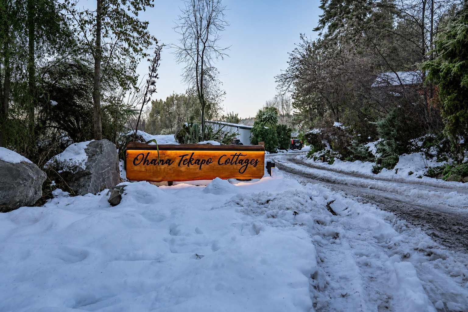 Ein verschneiter Weg führt zu einem Schild für Ohana Tekapo Cottages.