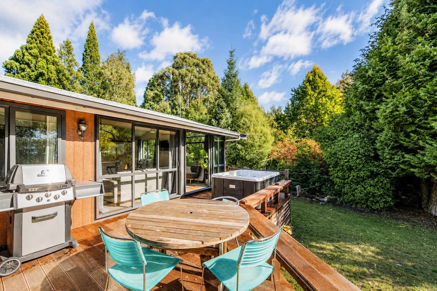A modern outdoor kitchen with a grill, hot tub, and dining area with wooden furniture.