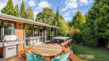 A modern outdoor kitchen with a grill, hot tub, and dining area with wooden furniture.