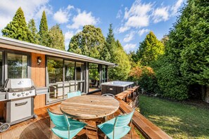 Une cuisine extérieure moderne, dotée d’un barbecue, d’un jacuzzi et d’un espace repas avec des meubles en bois.