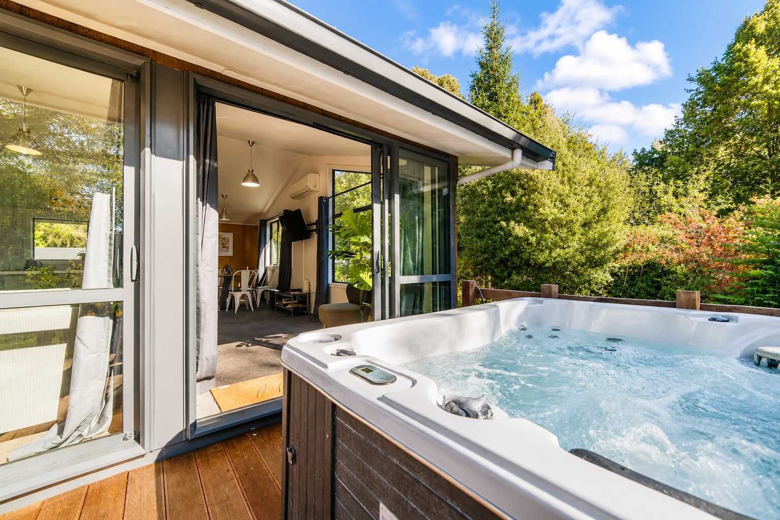 Un espace moderne aménagé à l’extérieur avec un bain à remous, une terrasse en bois, une porte vitrée donnant sur un patio et une vue sur un jardin luxuriant.