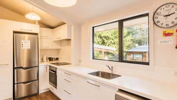 A modern kitchen with stainless steel appliances, white cabinetry, a double sink, and a large window with a view of the outdoors.