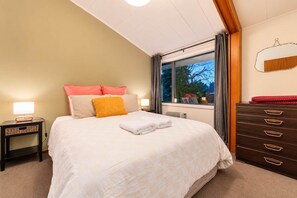 Une chambre à coucher avec un lit, des tables de chevet, une commode et une fenêtre avec des rideaux.