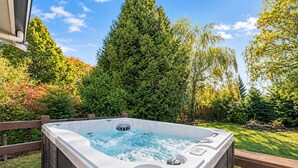 Ein Whirlpool auf einer Holzterrasse mit Blick auf einen üppigen Garten und hohe Bäume.