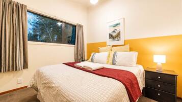 A hotel room with a bed, a nightstand, a lamp, a window with curtains, and a painting on the wall.