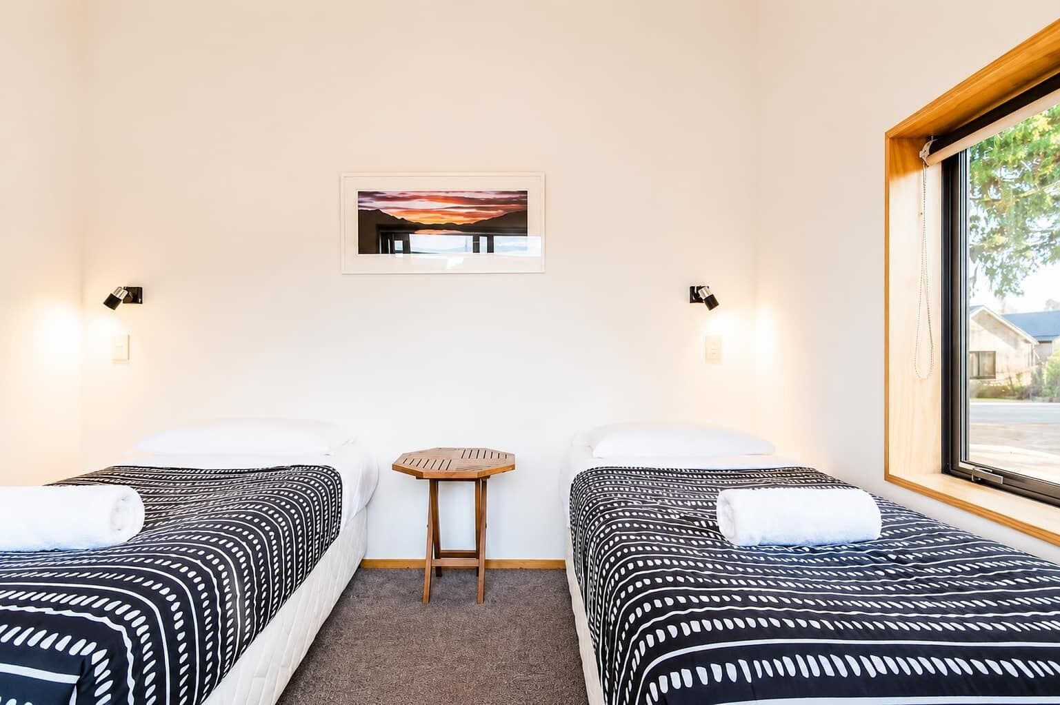 A hotel room with two beds, a small table, and a window with a view.
