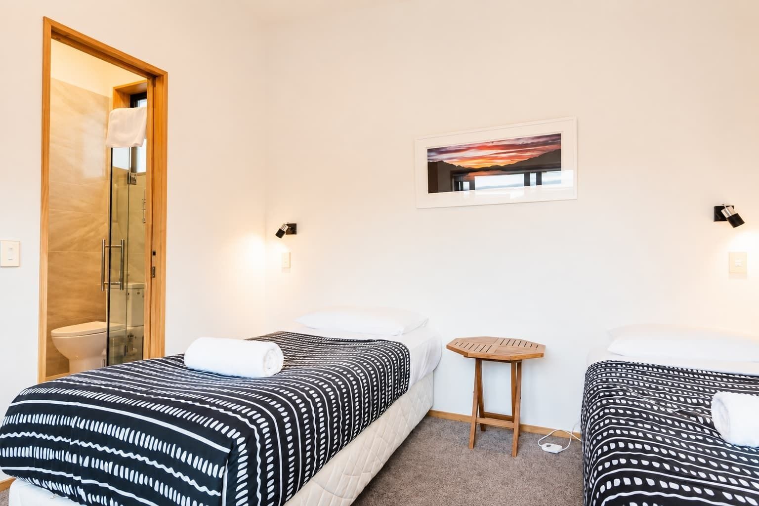 Una camera d'albergo con due letti, un tavolino, una doccia e un quadro appeso al muro.