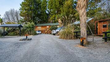 A gravel driveway leading to a wooden cabin with a metal roof, surrounded by tall trees and a small wooden structure.