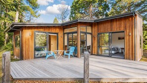 A modern wooden cabin with a deck, large sliding glass doors, and a visible bedroom with a bed.