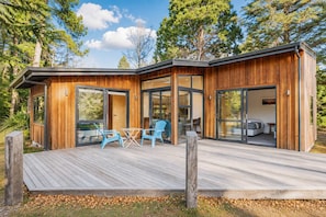Una cabaña de madera moderna con terraza, puertas correderas de vidrio grandes y un dormitorio visible con cama.