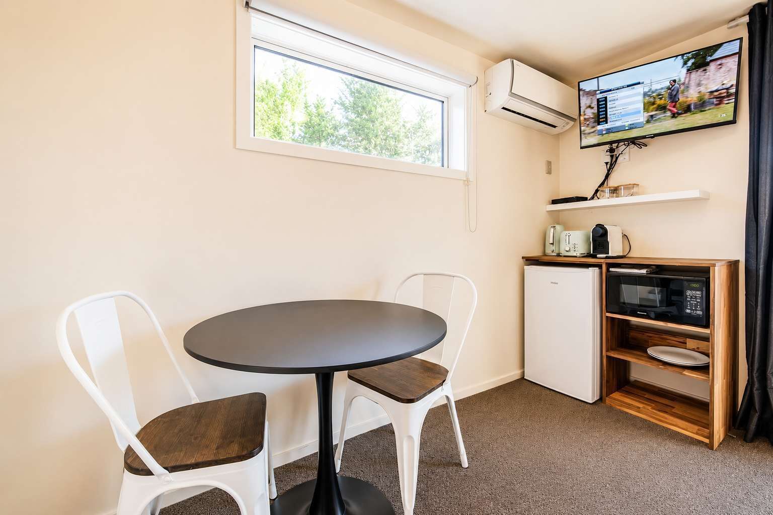 Ein gemütlicher Raum mit rundem Tisch und zwei Stühlen, eine kleine Küchenzeile mit Mikrowelle und Toaster sowie ein an der Wand befestigter Fernseher.