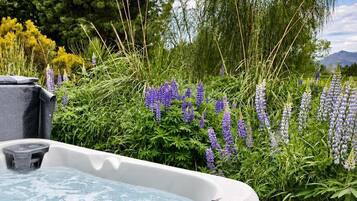 A hot tub with a control panel, surrounded by lush greenery and flowering plants.