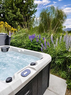 A hot tub with a control panel, surrounded by lush greenery and flowering plants.