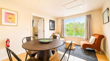 A dining area with a round table, chairs, a fire extinguisher, and a window with a view of greenery.
