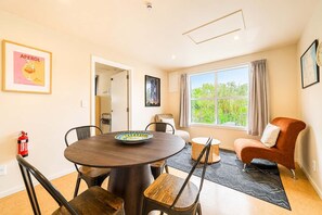 A dining area with a round table, chairs, a fire extinguisher, and a window with a view of greenery.