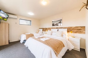 Quarto de hotel com duas camas, televisão, cabeceira de madeira, mesa de cabeceira com abajur e um quadro na parede.