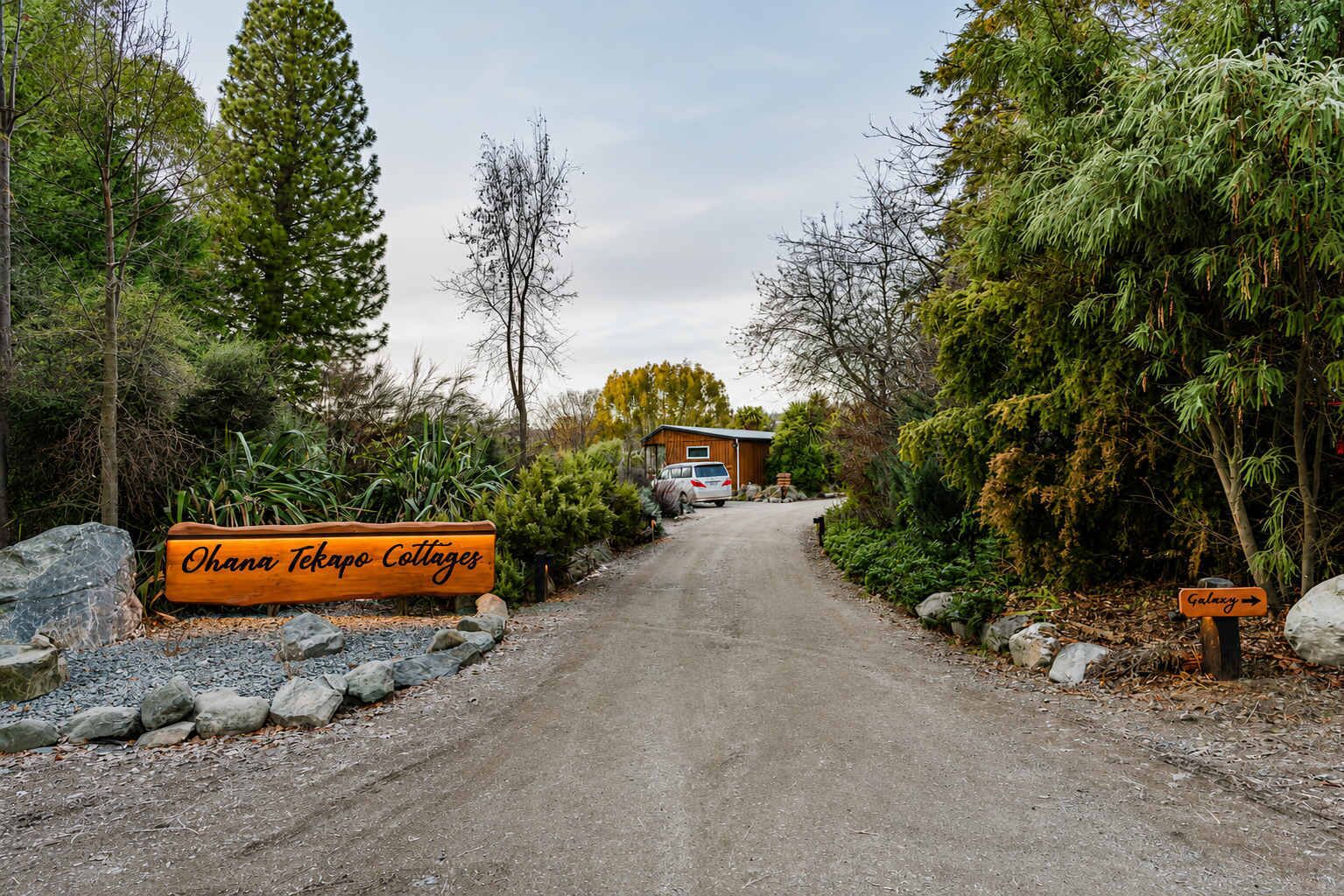 Ein Schotterweg führt zu einem Holzhaus mit einem Schild, auf dem 'Ohana Tekapo Cottages' steht.