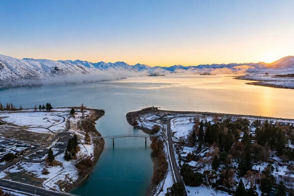 A snow-covered landscape with a bridge, a river, and mountains in the background.