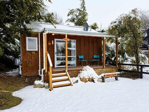 A wooden cabin with a covered porch, a sliding glass door, and two chairs outside.