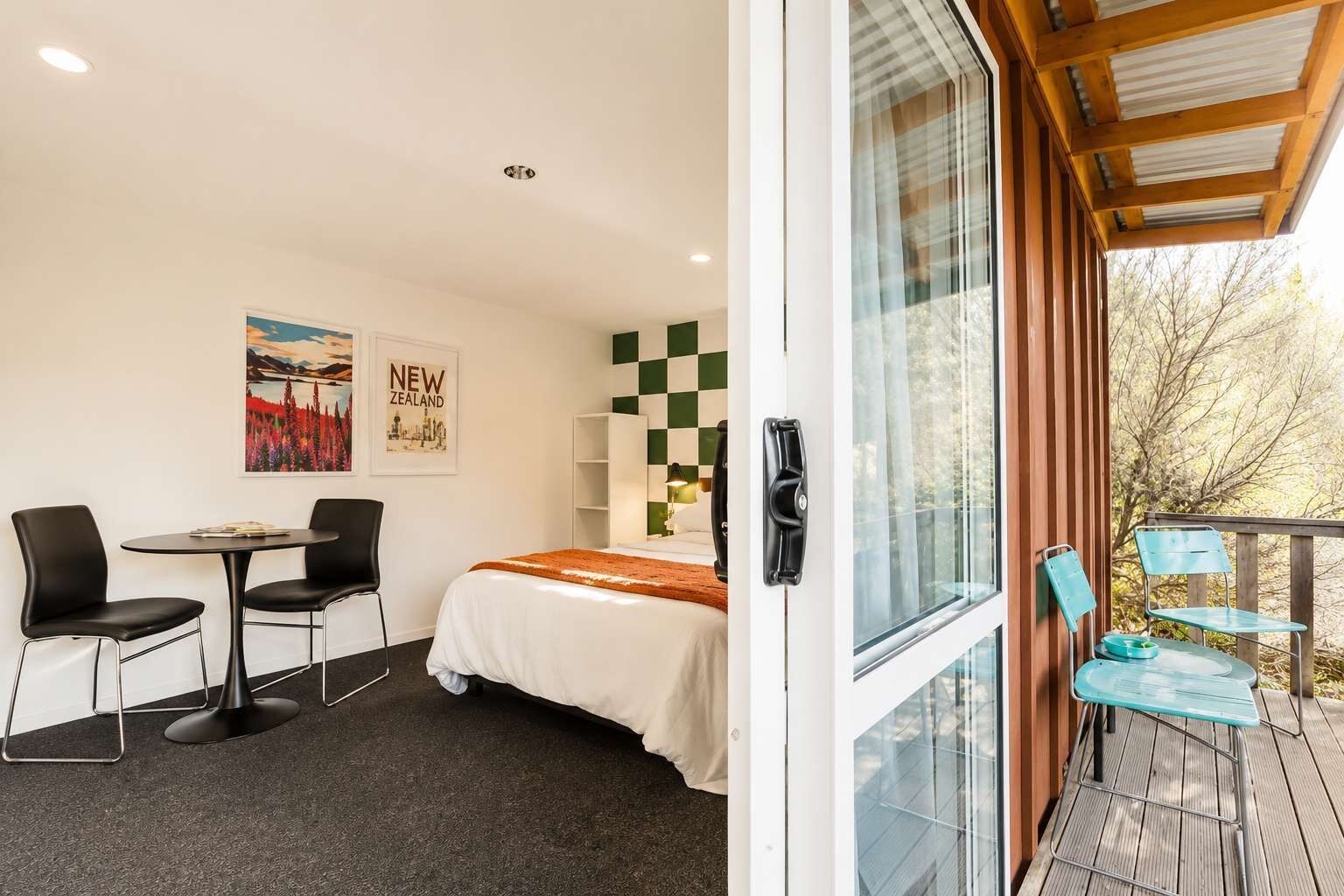 A room with a bed, a desk, two chairs, a window, and a view of trees.