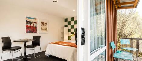 A room with a bed, a desk, two chairs, a window, and a view of trees.