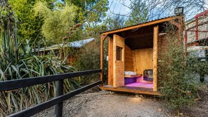 A small wooden cabin with a single bed, a table, and a bench.