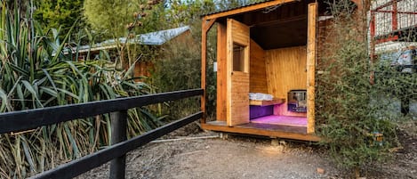 A small wooden cabin with a single bed, a table, and a bench.