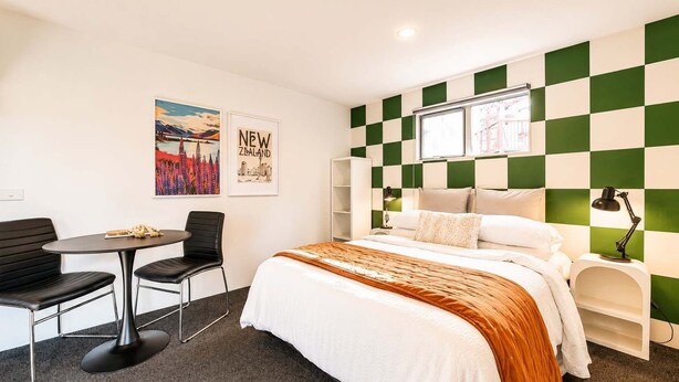 A hotel room with a bed, a desk with a chair, a window, and a wall with a checkered pattern. - Polaris | Lake Tekapo | Near Church + Balcony (Lake Tekapo)