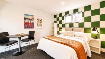 Habitación de hotel con cama, escritorio con silla, ventana y pared con diseño a cuadros.