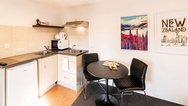 A compact kitchen with a microwave, kettle, and toaster, a small dining table with chairs, and a 'New Zealand' poster on the wall.