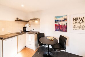 Une cuisine compacte équipée d’un four à micro-ondes, d’une bouilloire et d’un grille-pain, une petite table à manger avec des chaises, et une affiche représentant la « Nouvelle-Zélande » accrochée au mur.
