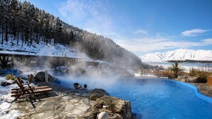A hot spring with a stone pool, wooden lounge chairs, and a forested mountain backdrop. - Polaris | Lake Tekapo | Near Church + Balcony (Lake Tekapo)