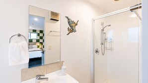 A modern bathroom with a glass shower enclosure, a white sink, and a mirror reflecting a room with a bed and a green and white checkered wall. - Polaris | Lake Tekapo | Near Church + Balcony (Lake Tekapo)